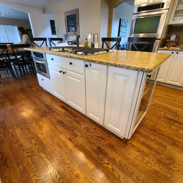 White kitchen island with granite counter and oak floors