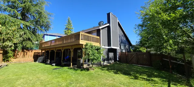 Dark gray A-frame house with cedar deck under a blue sky