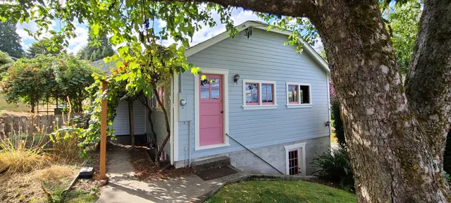 Light blue cottage with a pink front door beneath a large tree