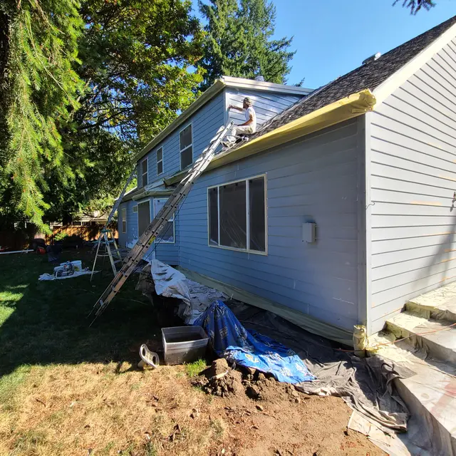 Painter working at the gable of a two-story house from the roofline