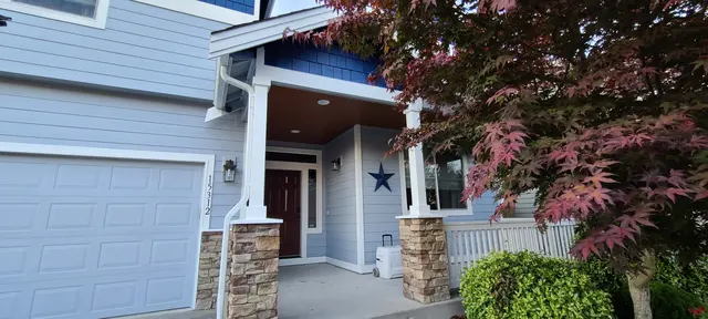 White garage and covered porch with stone accents and red maple